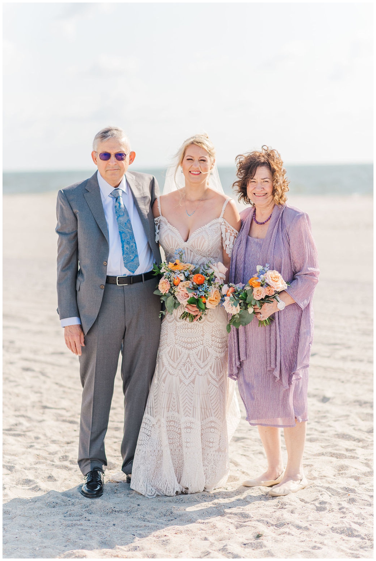 bride posing with her parents on the beach