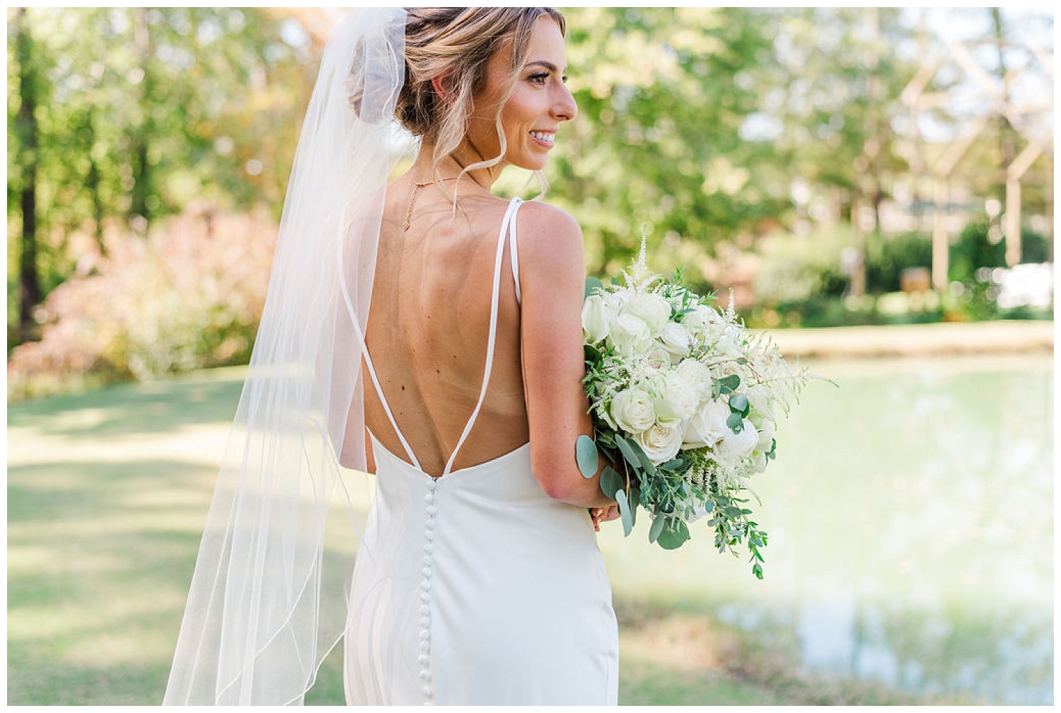 bride looking over her shoulder next to a pond at the Chapel Hill Carriage House