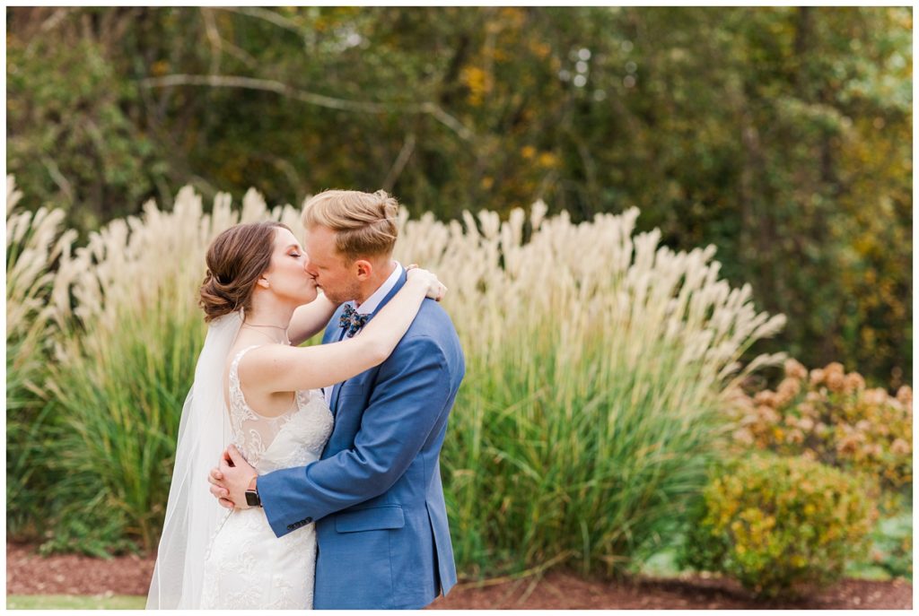 bride and groom kissing in front of tall grass at fall wedding