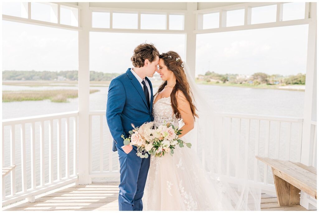 bride and groom standing under a white and blue gazebo on the beach