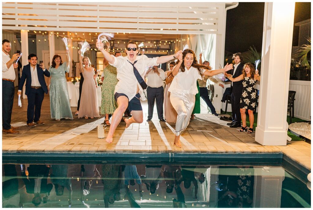 bride and groom jumping into pool at beach house reception
