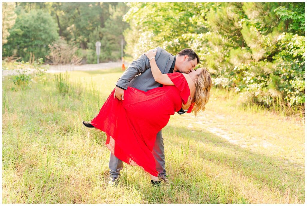man dipping back woman for kiss in a field engagement session