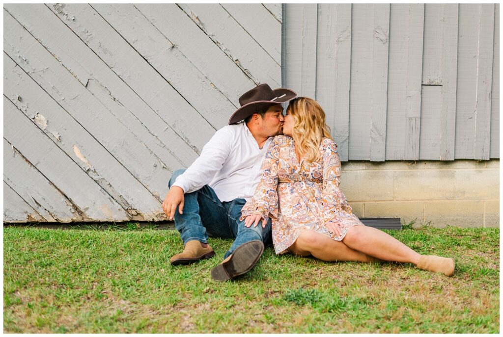 couple sitting in front of a gray barn for engagement session