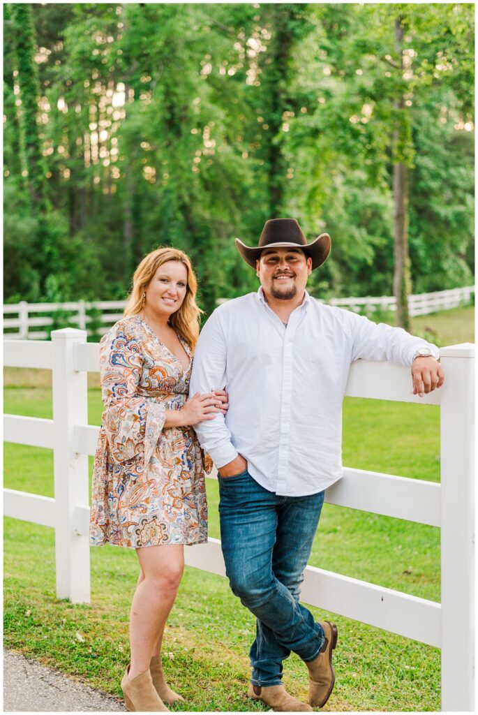 engaged couple standing in front of a white fence on a farm