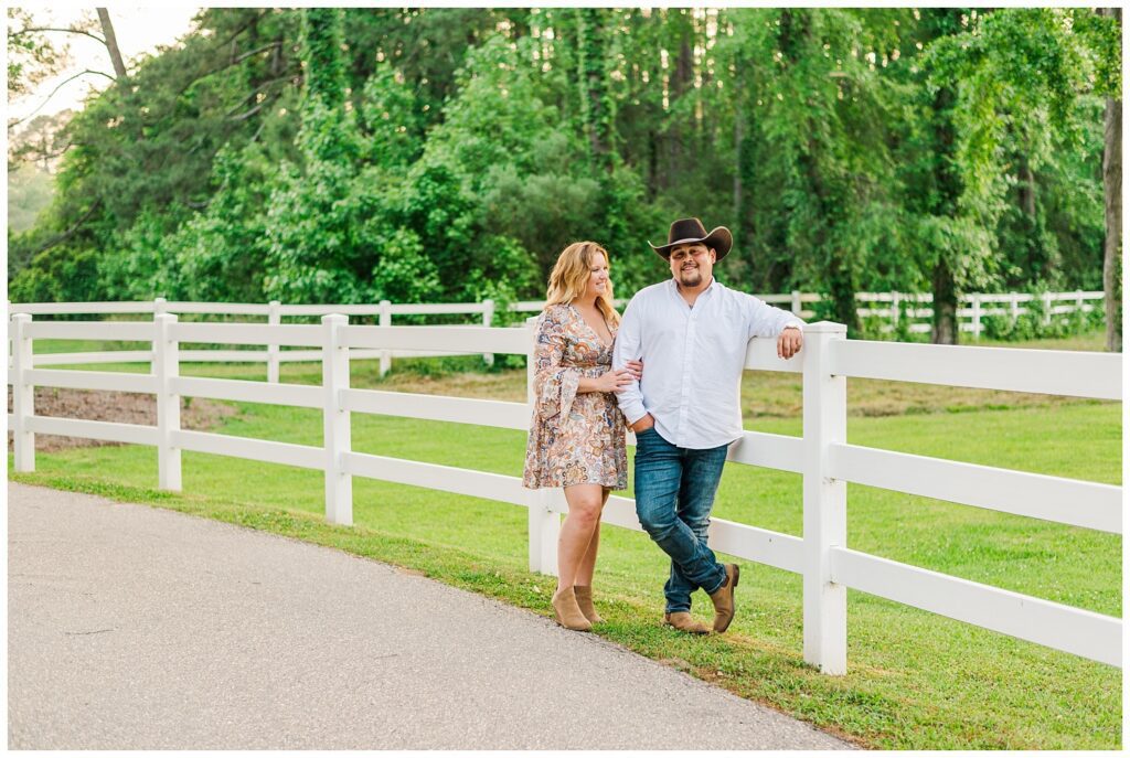 engaged couple standing in front of a white fence on a farm