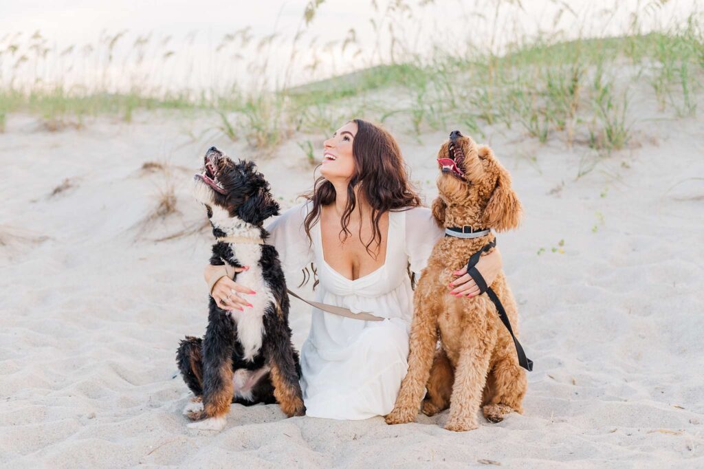 dog owner wearing a white dress looking up with her dogs on the beach
