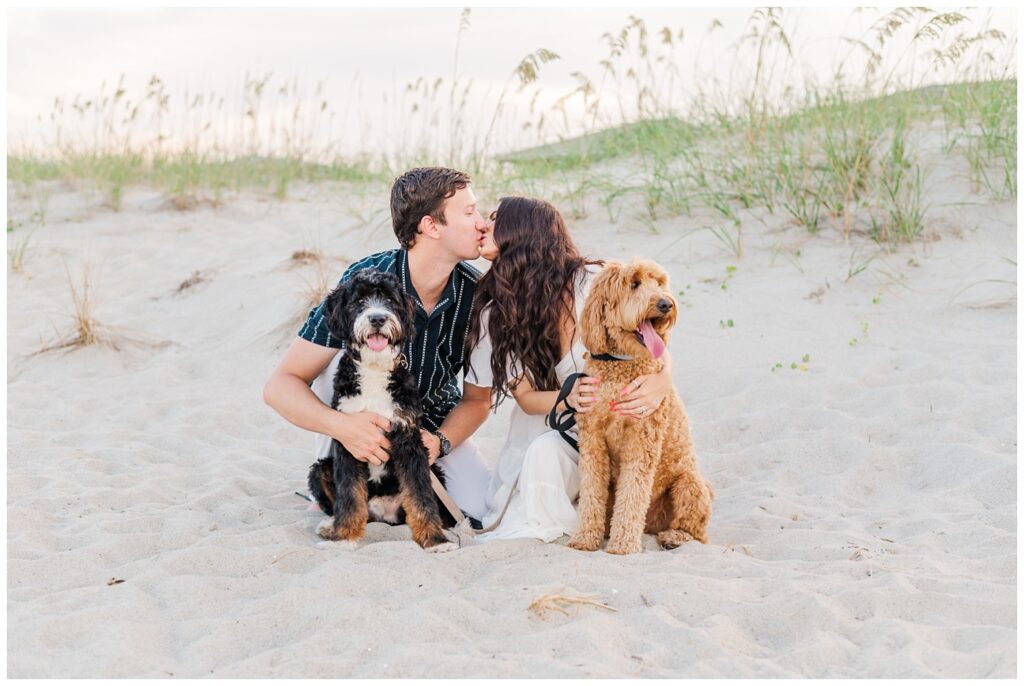 couple kissing while holding their dogs on the beach in North Carolina