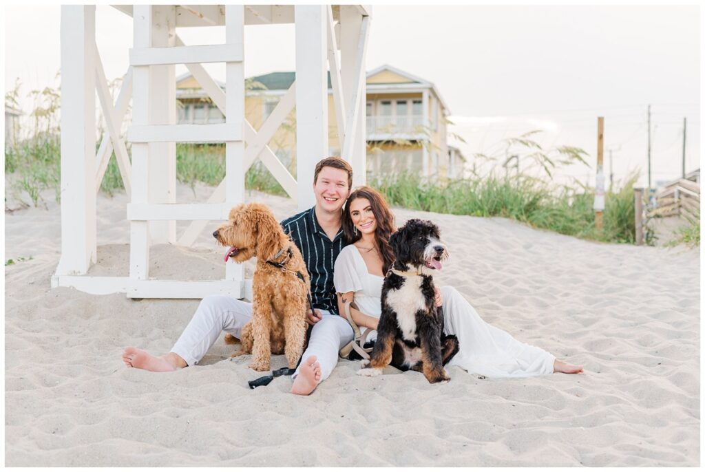 engagement couple sitting on the beach in Wilmington with their dogs