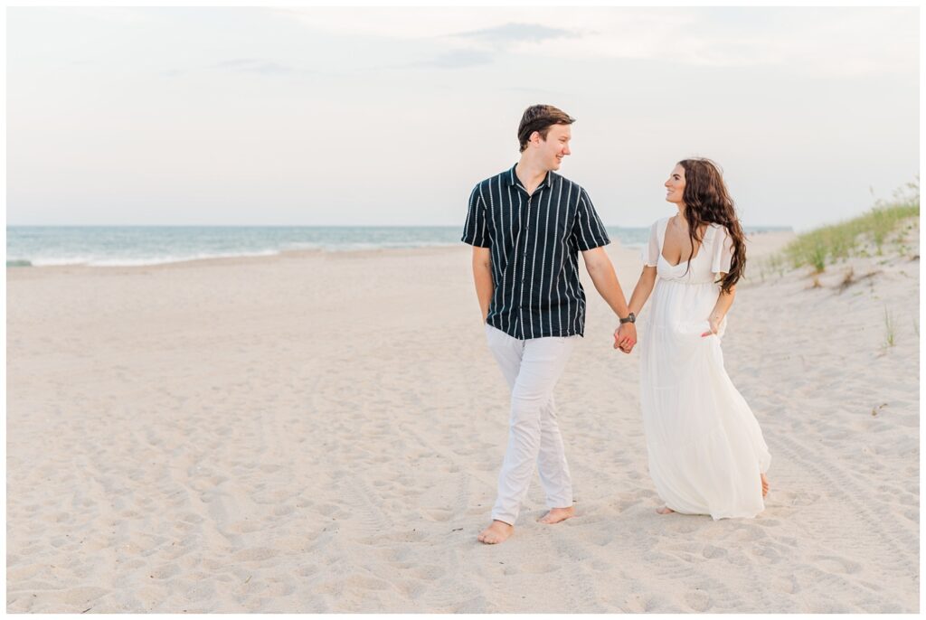 couple wearing white and navy walking on the beach for engagement session