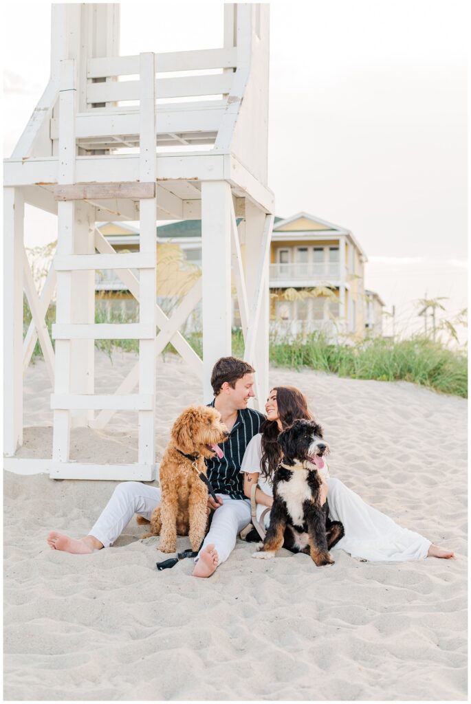 couple posing with their dogs in front of a lifeguard stand on the beach