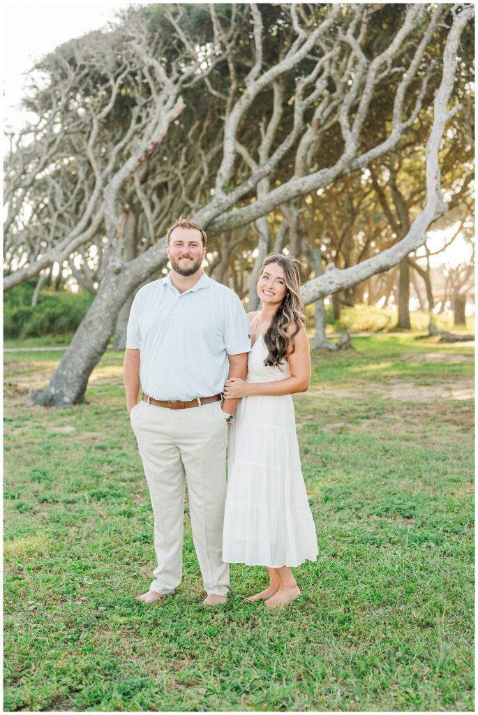 engaged couple standing in front of a large tree at Fort Fisher
