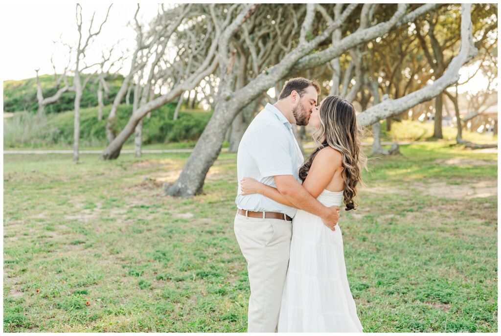 engagement couple kissing in front of a large tree at Fort Fisher, NC