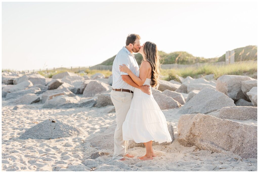 engaged couple kissing on the beach near the rocks at Fort Fisher, NC
