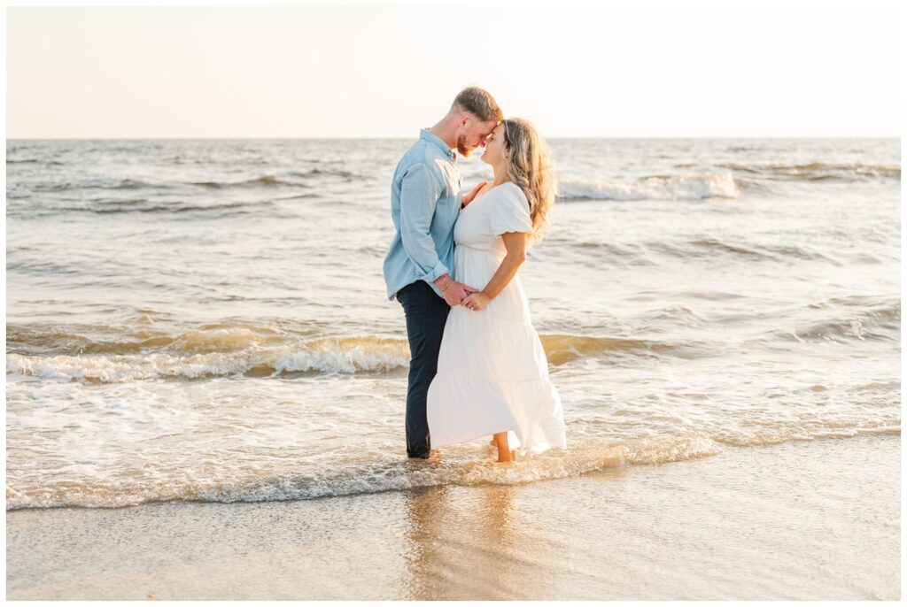 couple standing in the ocean for beach engagement session in Oak Island, NC