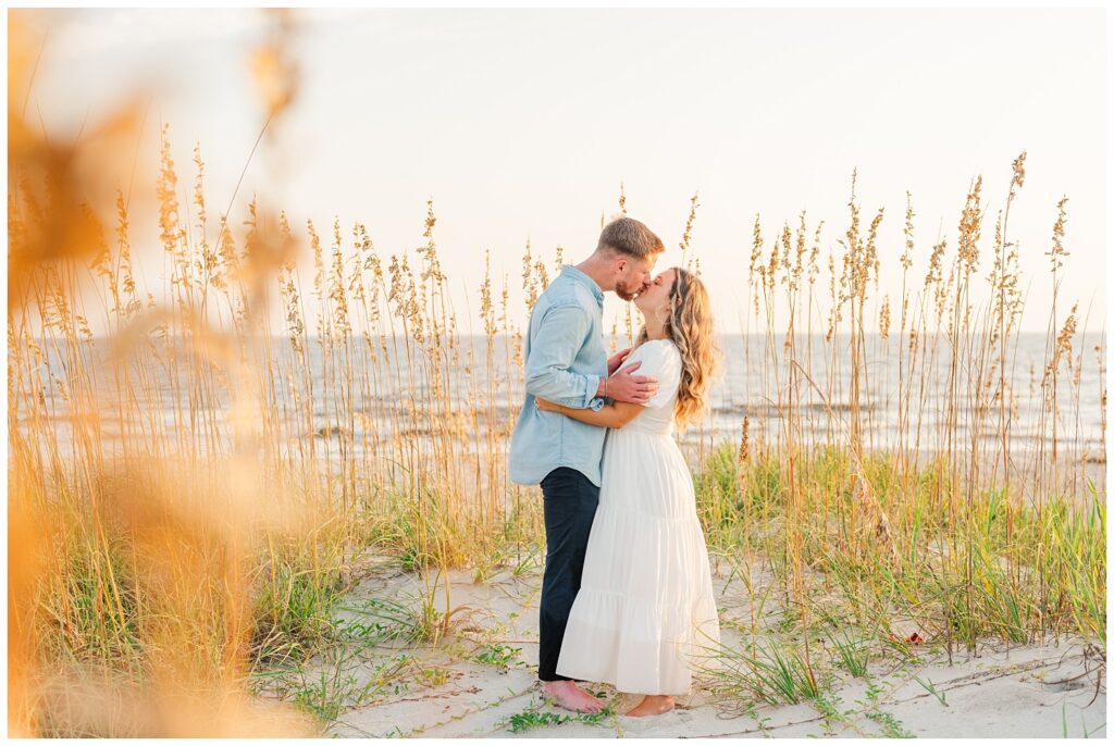 couple kissing next to sea grass on the beach in Oak Island, NC