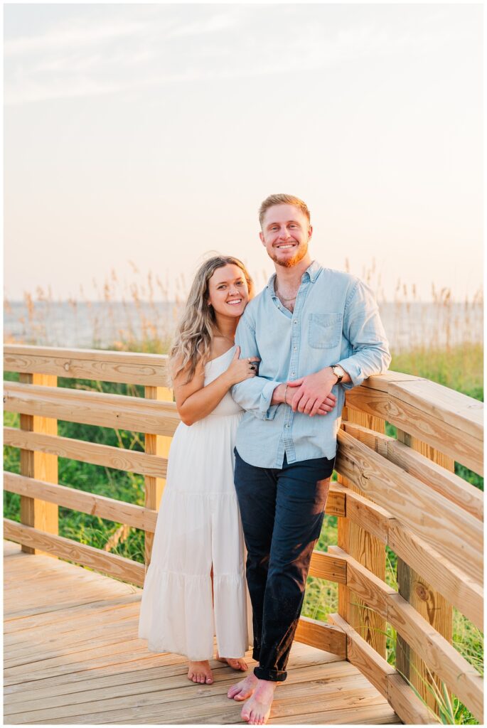 couple posing on a boardwalk for summer engagement session in Oak Island, NC