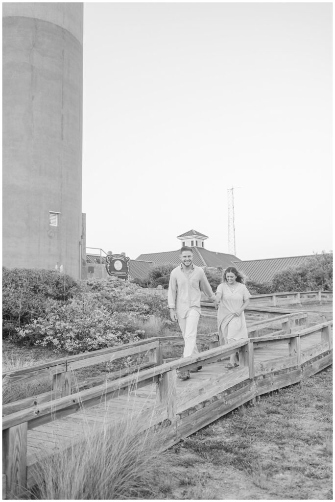 couple walking on a boardwalk near a lighthouse in Oak Island, NC