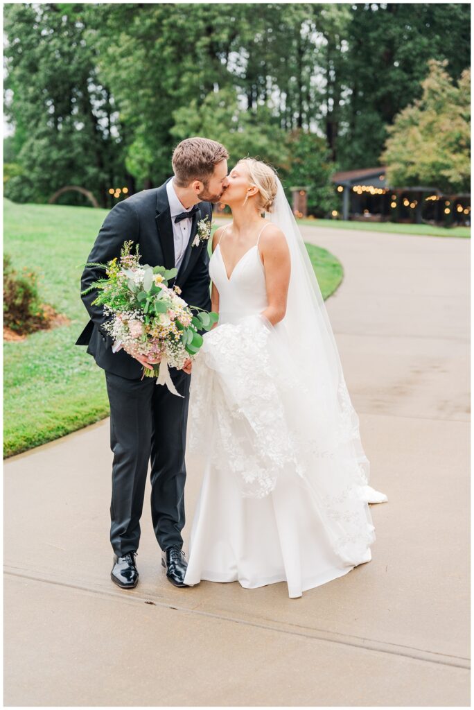 bride holding her train while groom gives her a kiss in the rain