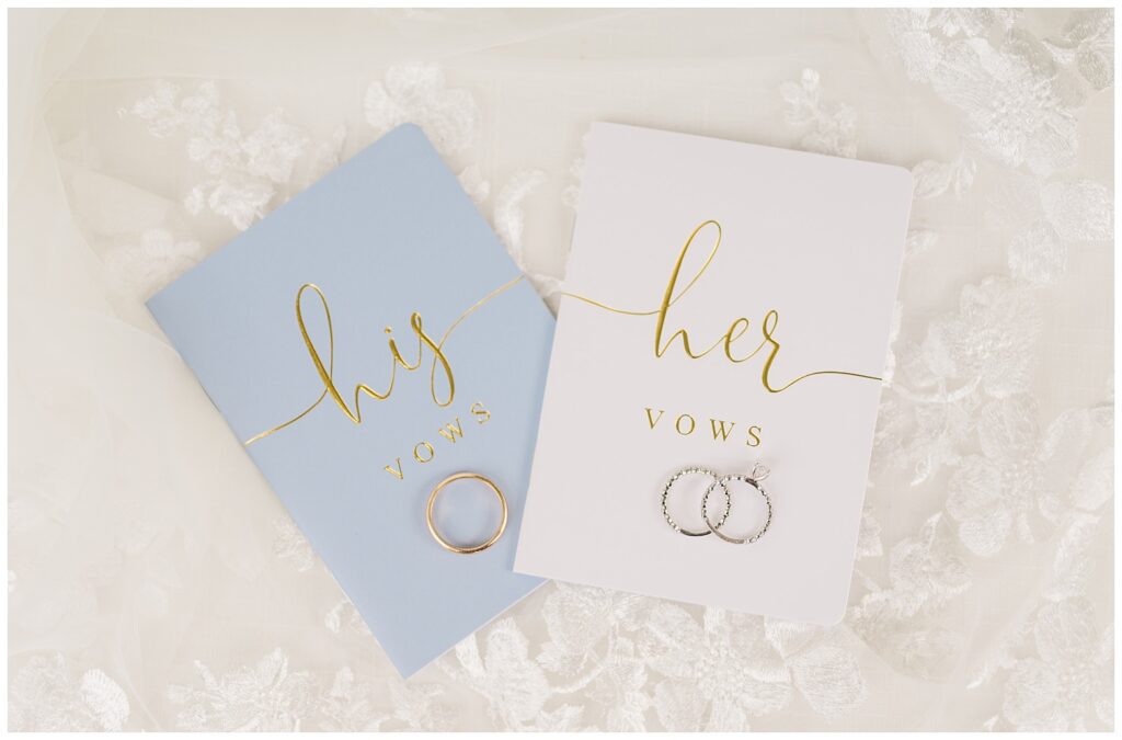 wedding rings sitting on top of white and blue vow books 