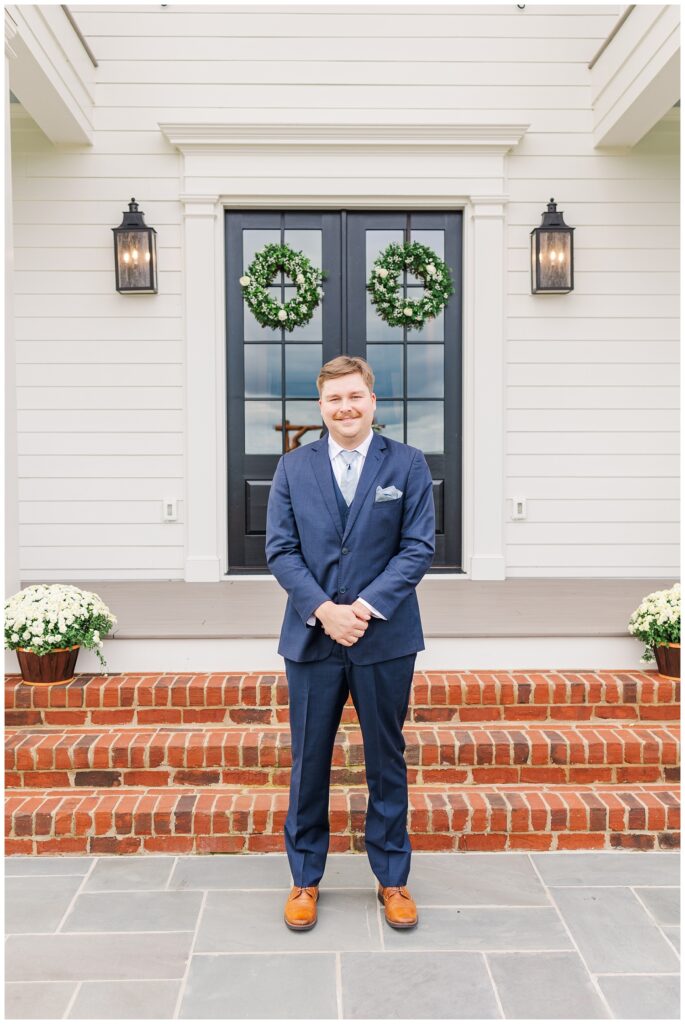 groom posing in front of two black doors with wreaths