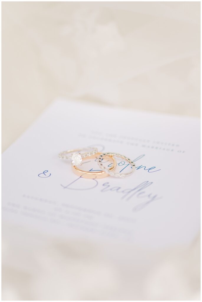 gold wedding rings sitting on top of a blue and white invitation flat lay