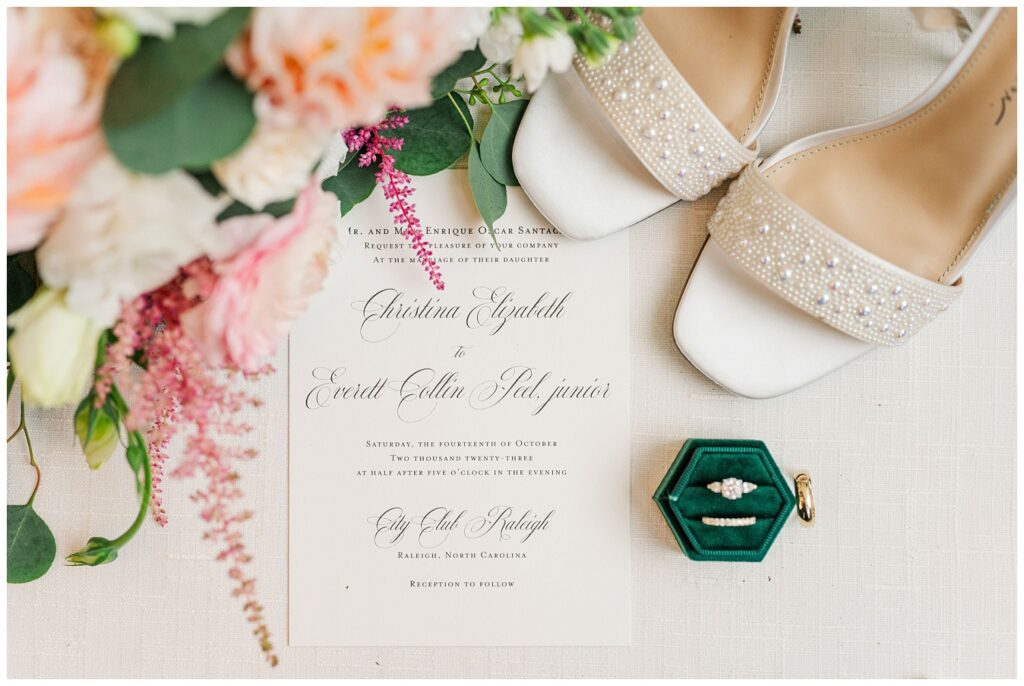flat lay with invitation, wedding shoes, flowers, and dark green velvet ring box