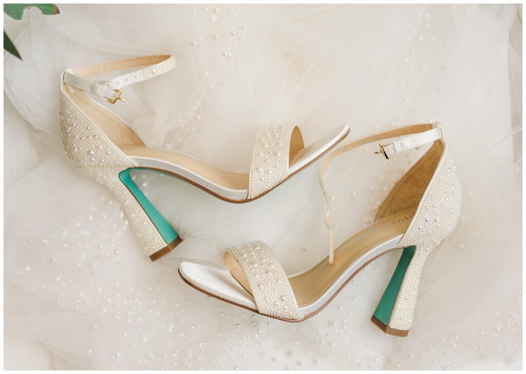 pearl studded wedding heels with Tiffany blue on the bottom sitting on top of her dress