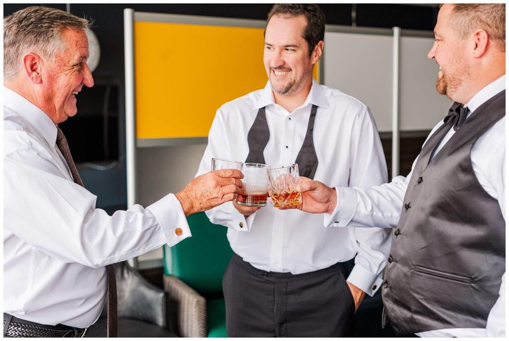 groom, dad, and groomsmen toast with whiskey while getting ready at the City Club Raleigh