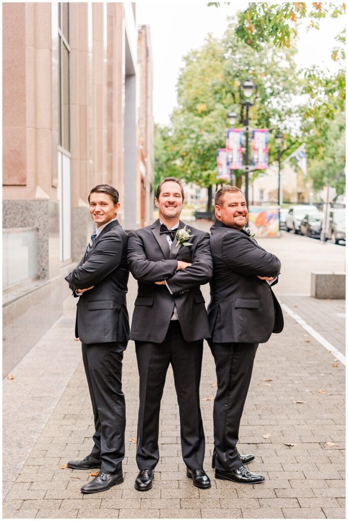 groomsmen posing on the sidewalk outside the City Club Raleigh wedding venue