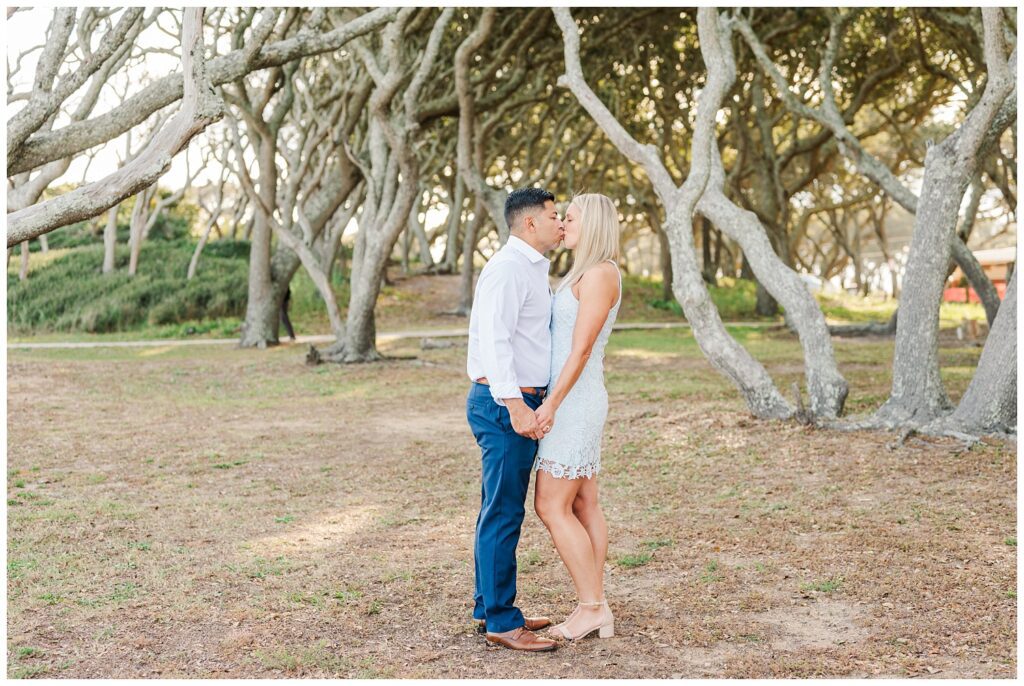 engagement couple kissing near some trees at Fort Fisher beach