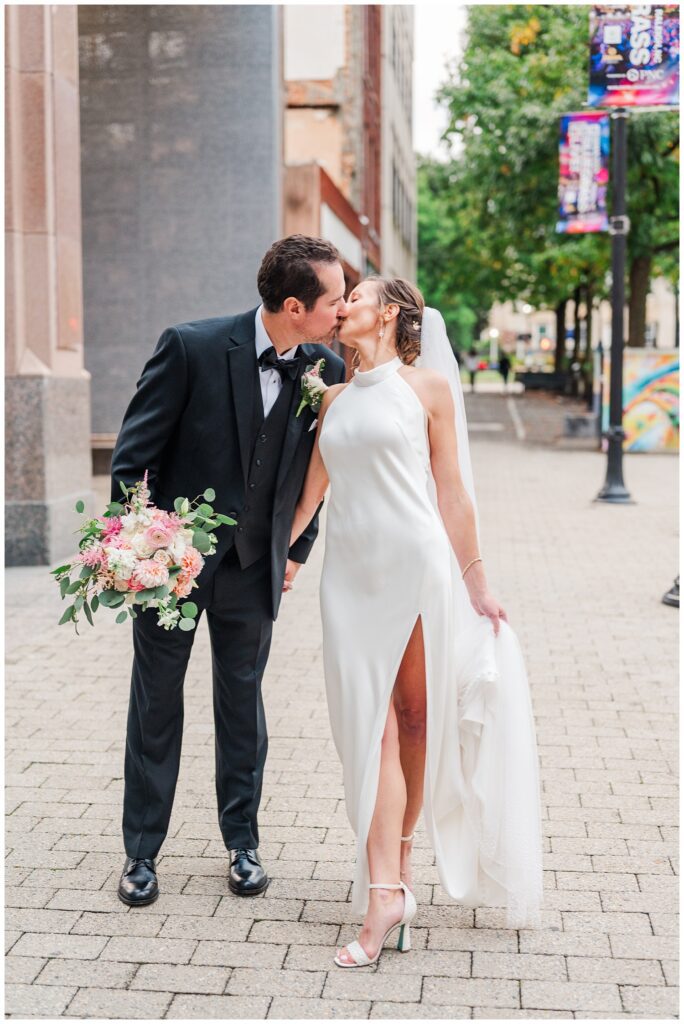 wedding couple share a kiss on the sidewalk in downtown Raleigh