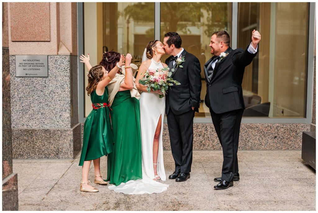 bride and groom share a kiss while posing with their attendants at wedding in Raleigh