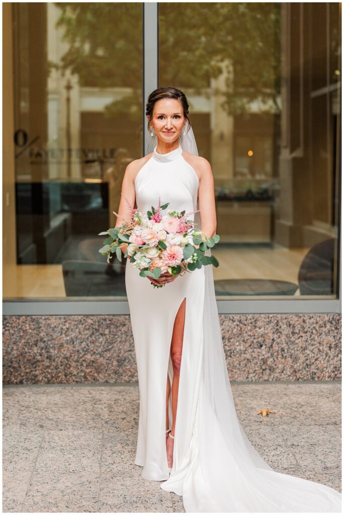 bride wearing a halter neck and high slit white wedding dress while posing with bouquet