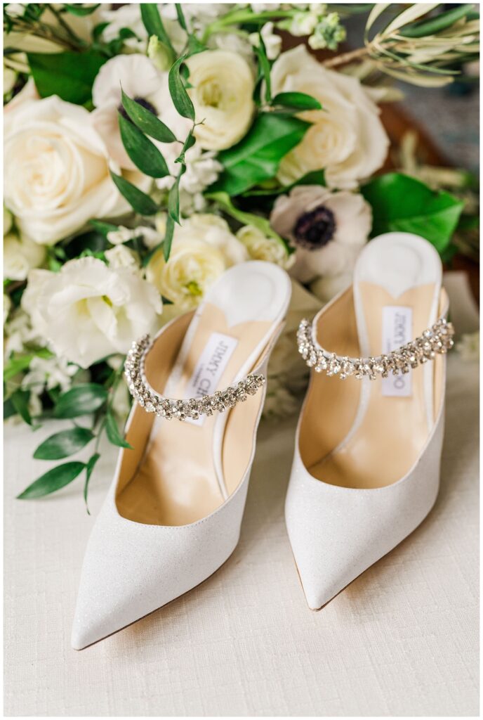 white Jimmy Choo wedding shoes sitting in front of florals made by Fiore Design House in Wilmington