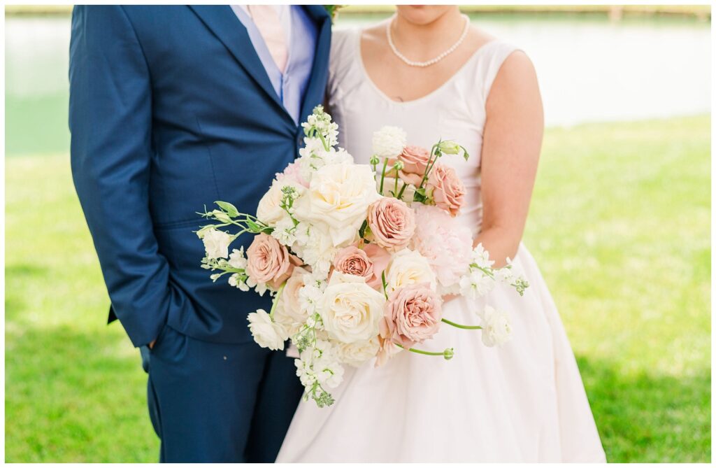 bride and groom posing next to a pond with close up of Wilmington wedding bouquet