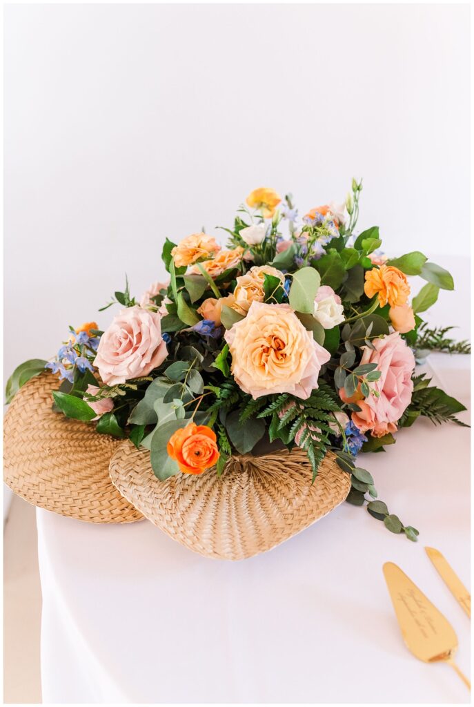 florals made by Serendipity Floral Designs sitting on top of wicker fans on cake table 