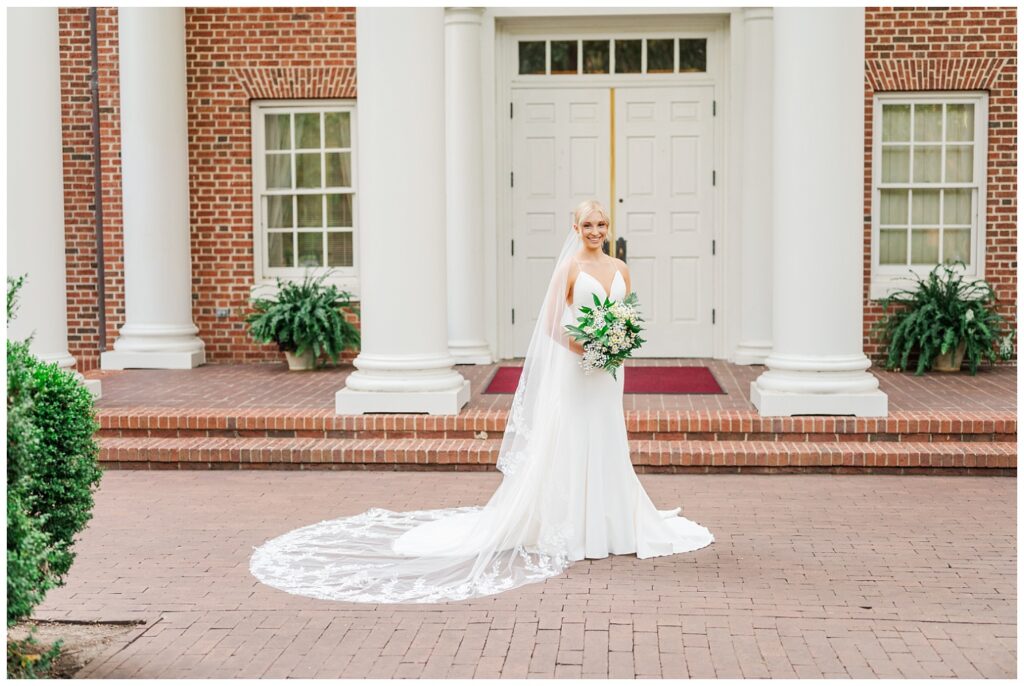 bride posing in front of a white column and brick building at Meredith College