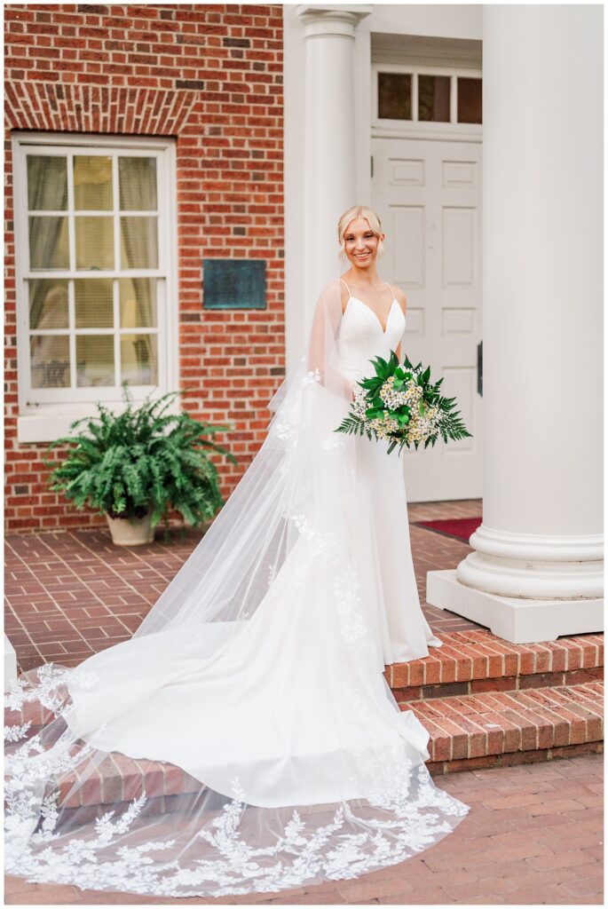 bride posing on the porch of a brick and white column building in Raleigh, NC