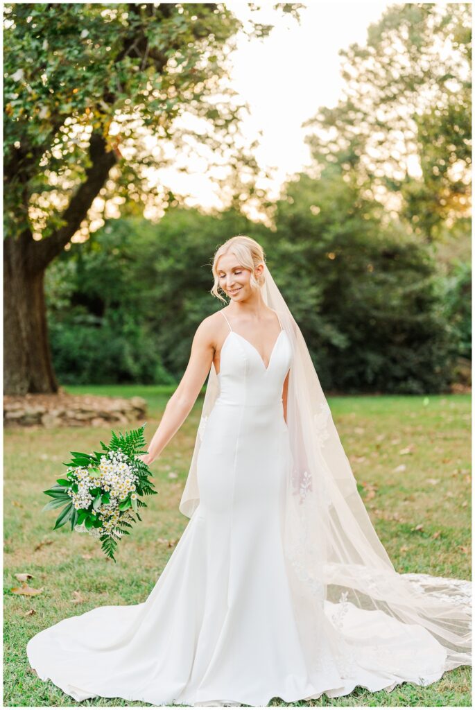 bride holding out her bouquet while posing on the grounds at Meredith College in Raleigh