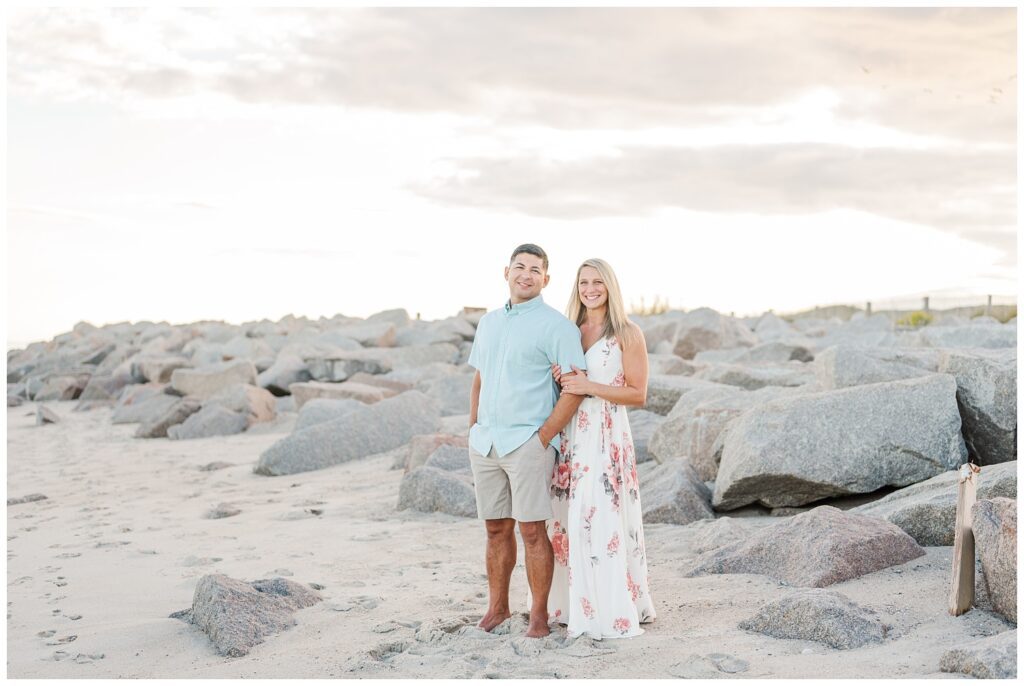 engaged couple standing on the beach next to the big rocks at Fort Fisher, NC