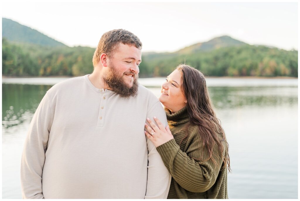 couple smiling at each other with the Virginia mountains and lake in the background