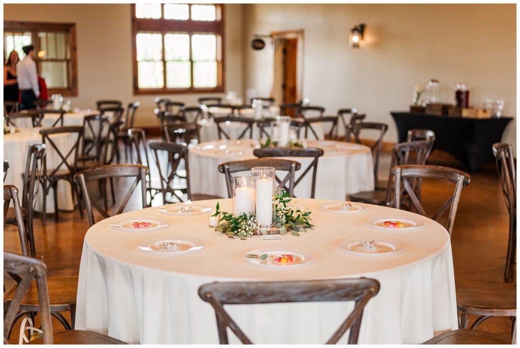 reception tables decorated with white candles, greenery, and hurricane vases