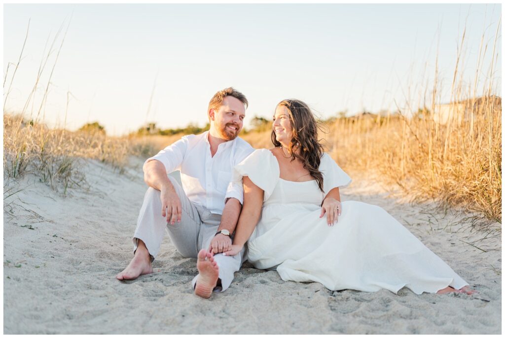 couple sitting on the sand during golden hour for engagement session