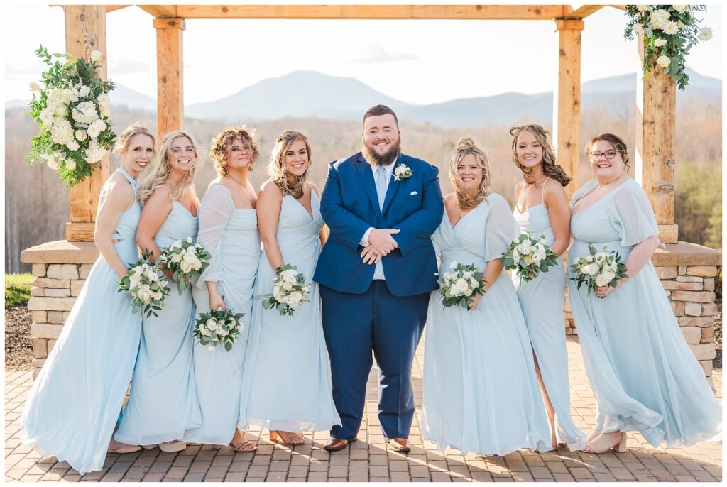 groom posing with the bridesmaids outdoors at the Glass Hill Venue