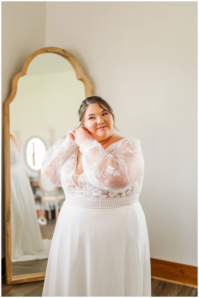 bride wearing a lace wedding dress and putting in her earrings 