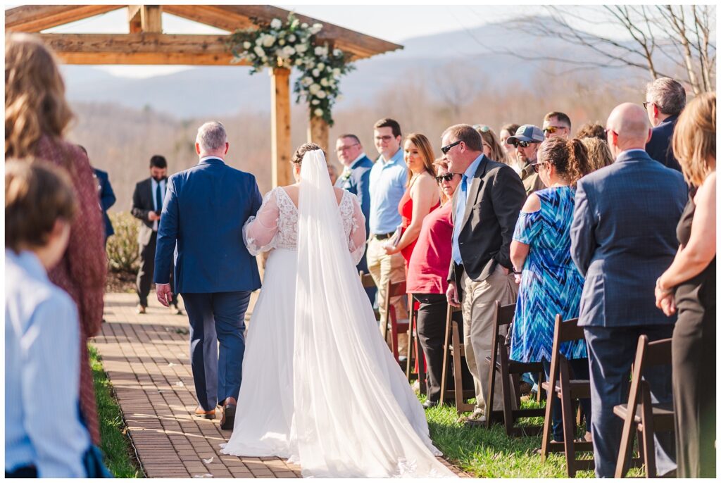 bride walking down the aisle with her dad as guests look on