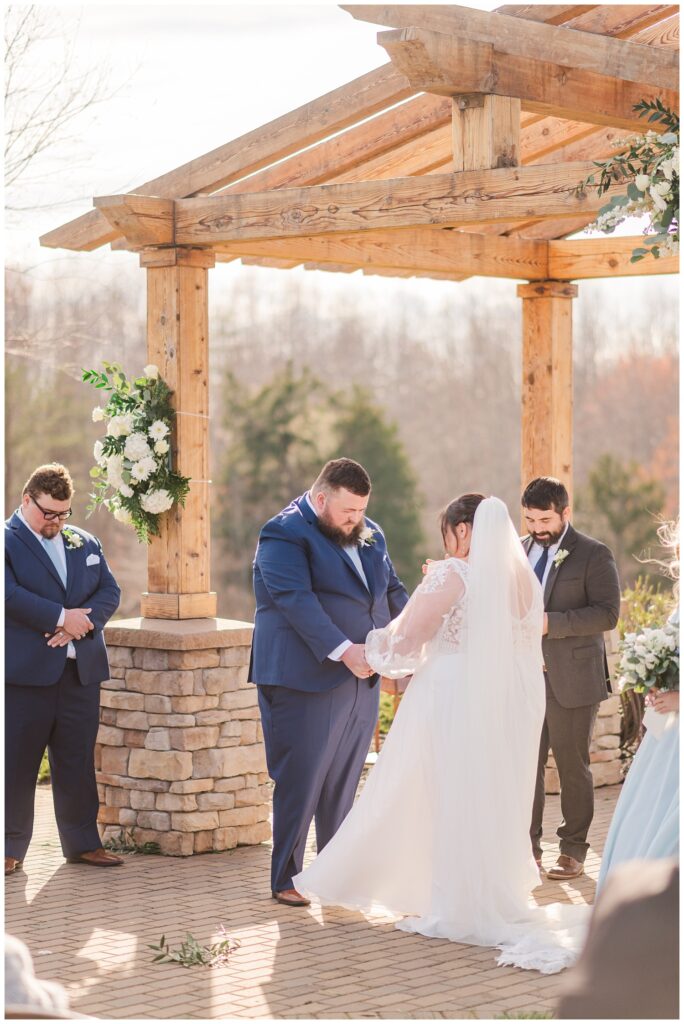 bride and groom holding hands and praying at the outdoor altar during ceremony 