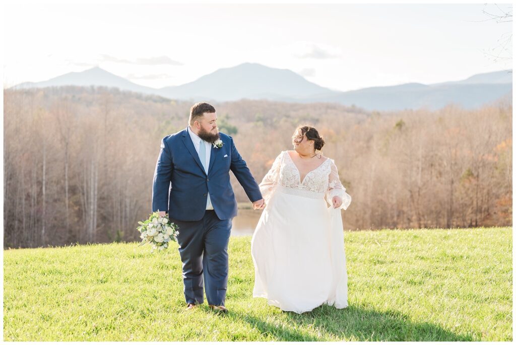 bride and groom walking hand in hand across the grass in front of the Virginia mountains