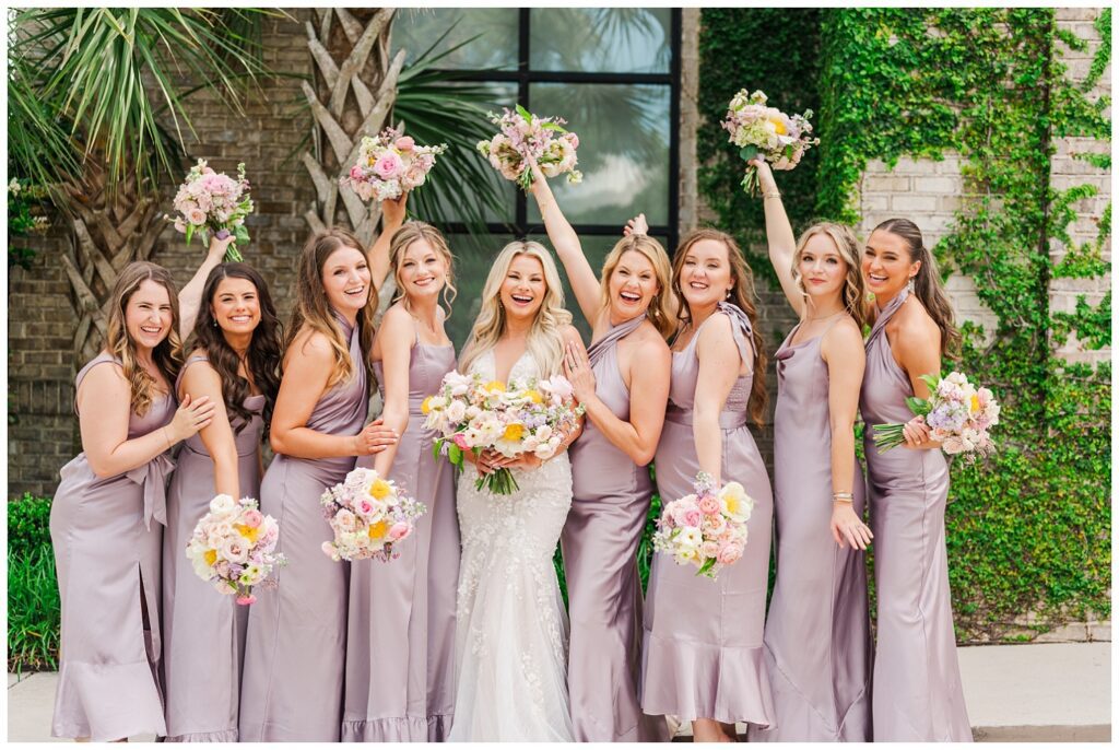 bridal party smiling and holding their bouquets in the air with the bride