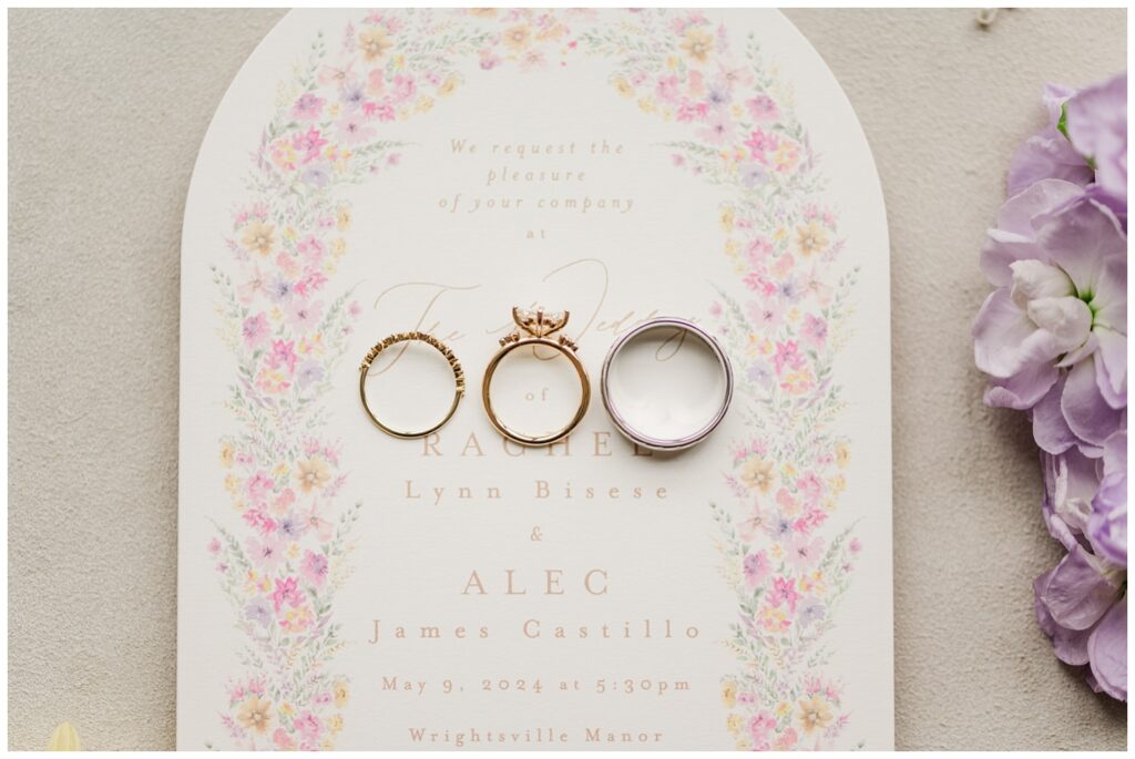 bride and groom's wedding rings sittng on top of an ivory and pink invitation